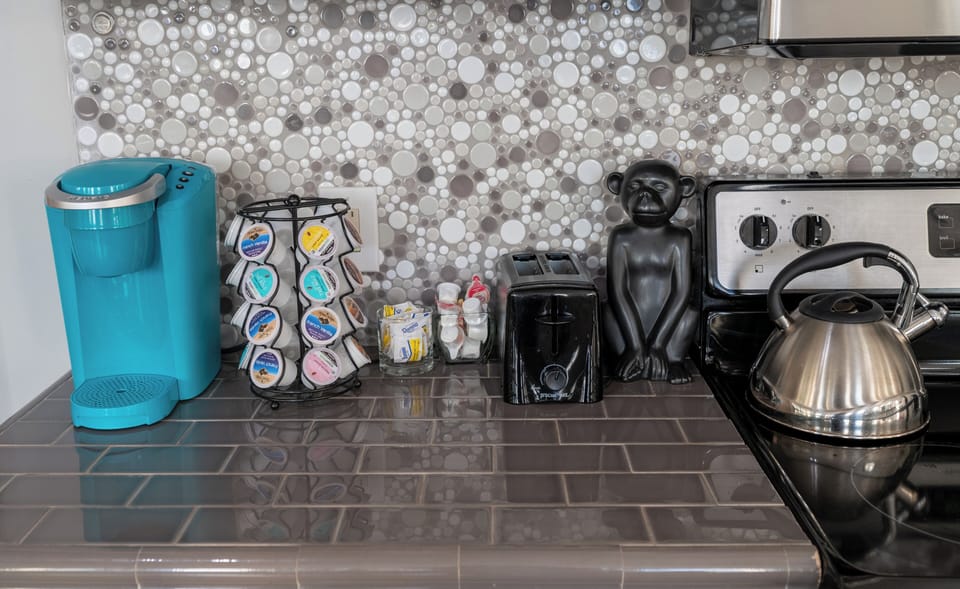 Cook with confidence: stainless appliances, glass-front cabinets, mosaic backsplash, chandelier sparkle, and a welcoming snack basket.