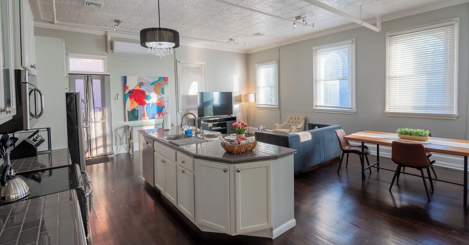 Airy, all-in-one living space with a centerpiece island, cozy sofa, and window-lined dining—perfect for slow breakfasts, easy dinners, and conversation.