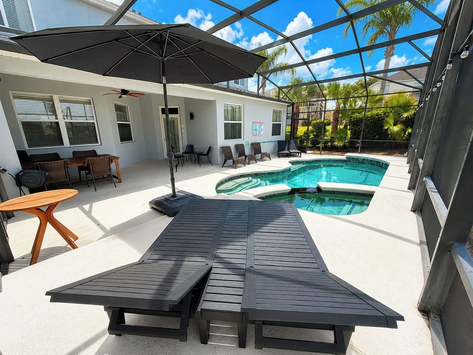 Pool deck showing double sun lounger, umbrella and outdoor dining area.
