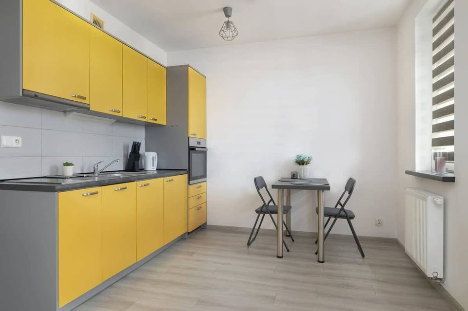 A spacious kitchen and dining area with bright yellow cabinetry, a gray backsplash, and modern design.

