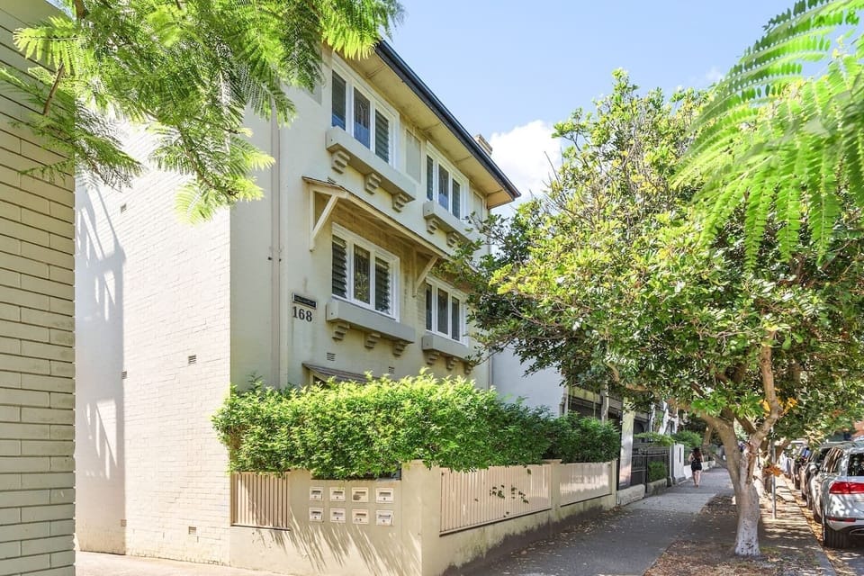 The apartment building maintains lush hedges outside and is situated on a leafy and picturesque street. 

