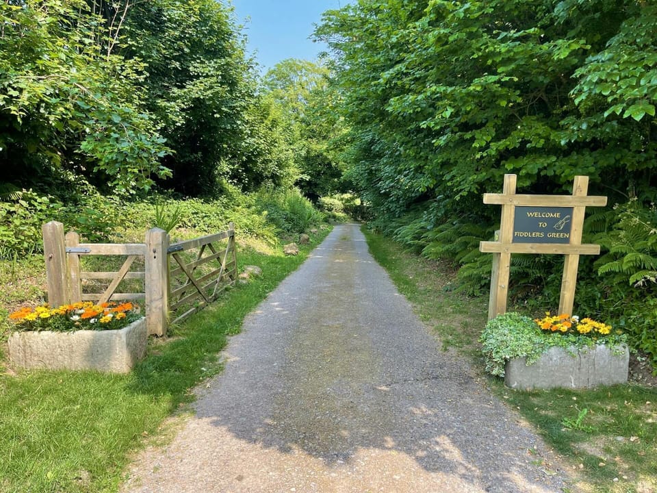 Entrance to Fiddlers Green, gravel driveway, entrance gate and stone planters with flowers