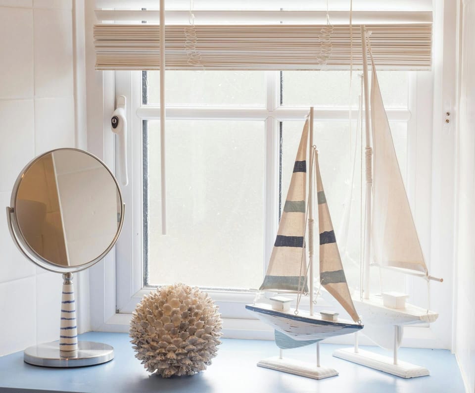 Window sill in bathroom with shaving mirror, sail boat ornaments, blind