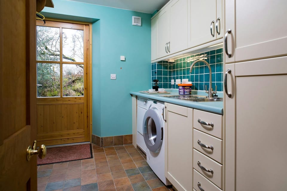 Utility room with washing machine, sink, fitted units, tiled floor, door to garden.