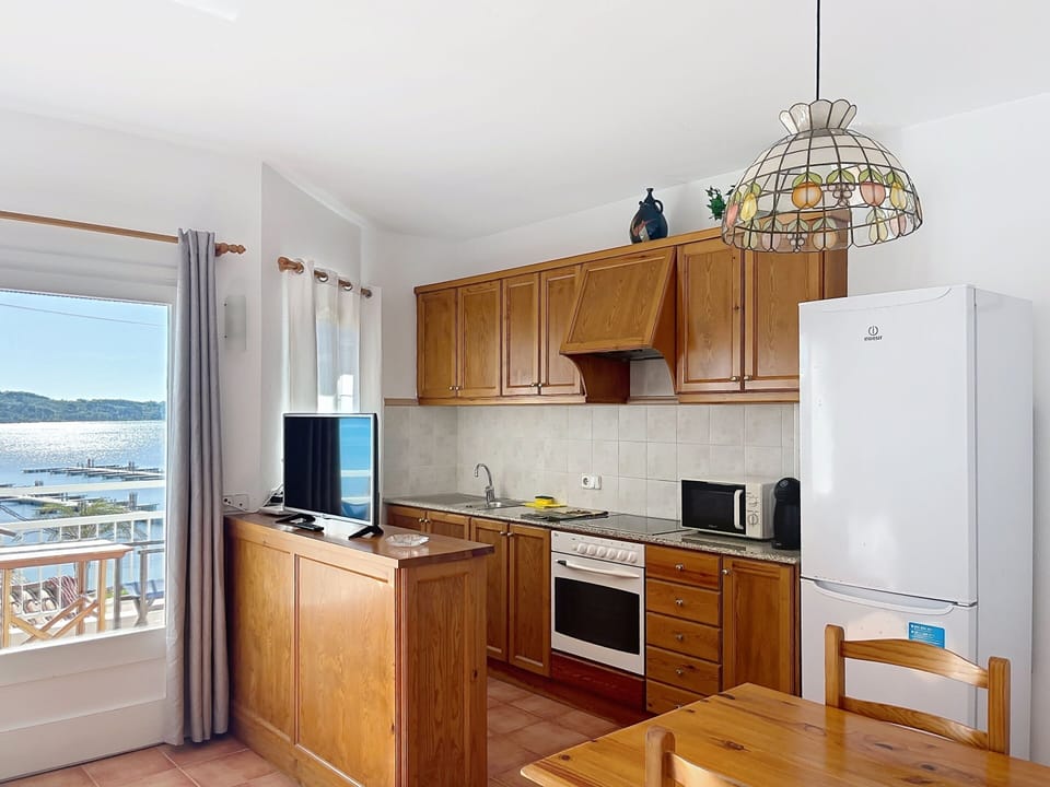 Open kitchen with sea views, fully equipped with oven, hob, microwave, large fridge/freezer, and Dolce Gusto coffee machine.