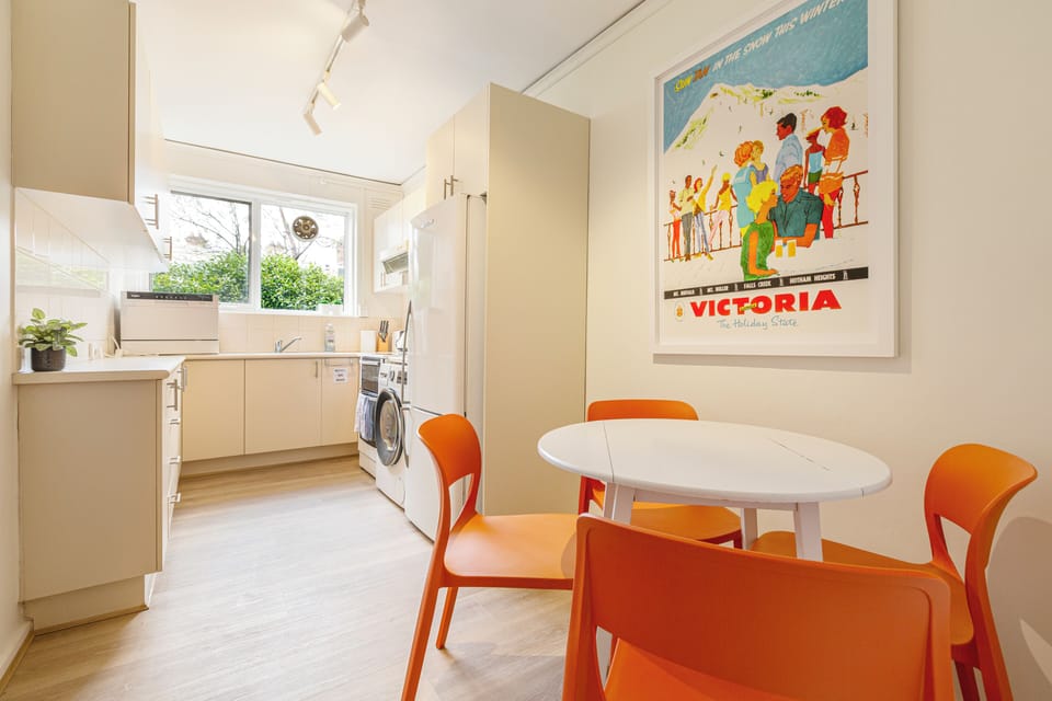 The dining table adjoins the kitchen and has a funky white round table with four vivid tangerine-toned seats.