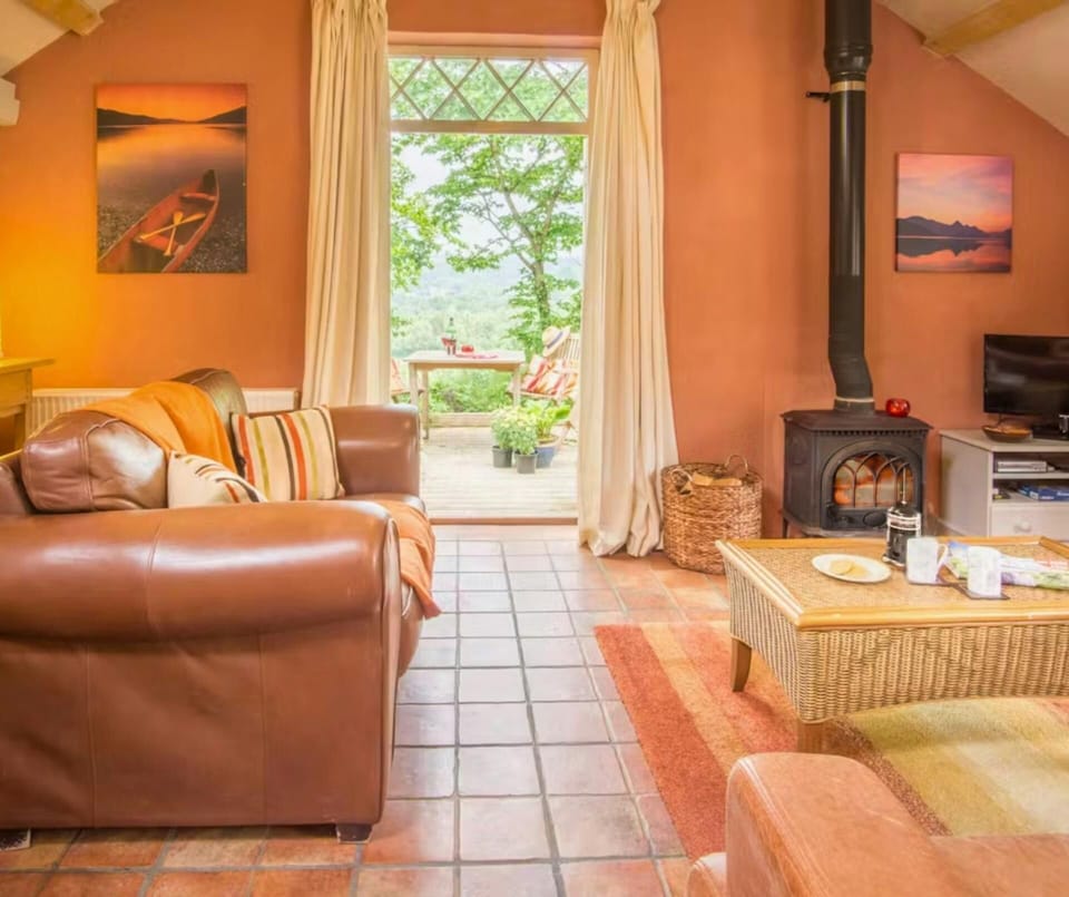Spacious living area with sofa, wicker coffee table, TV and log burner; external door leading to outside seating area