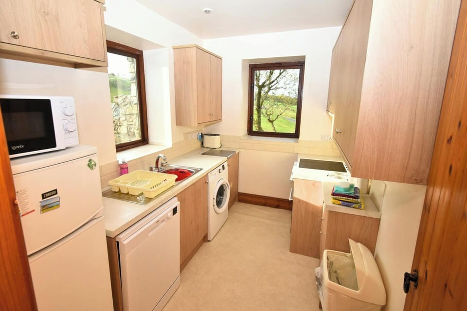 Small kitchen with two windows, wooden cabinetry, fridge and countertop appliances