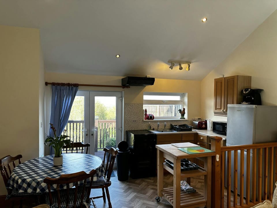 Dining table and four chairs, and kitchen area: fridge/freezer, cooker, microwave, kettle & toaster