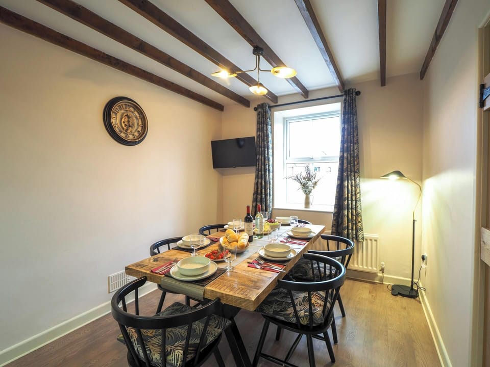 Table and six chairs laid for dinner. TV on the wall and standard lamp in the corner