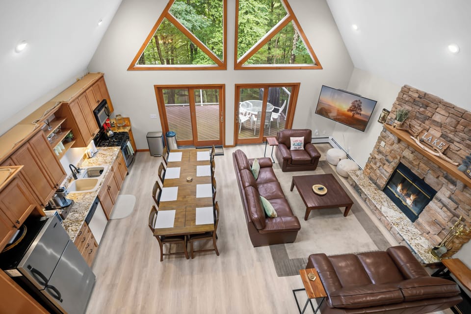 Open floor plan: Vaulted great room with forest views, stone fireplace, and access to elevated deck