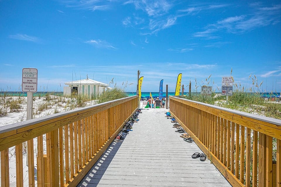 Wooden boardwalk leads to pristine white sand beach with clear blue waters and dunes.