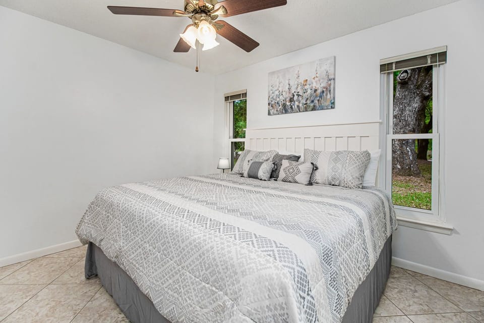 Find comfort in this inviting bedroom with a king-sized bed, chic gray bedding, and a picturesque window that offers a glimpse of the lush outdoors, creating a perfect haven for relaxation.