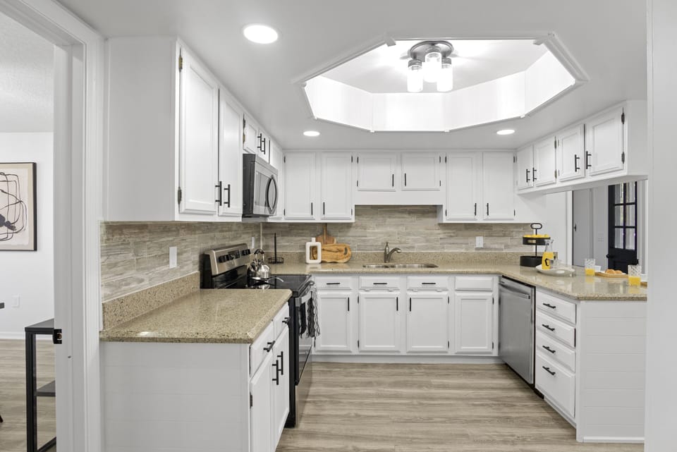 Spacious kitchen with cabinets, a four-burner stove and oven, microwave, kettle, and plenty of light.