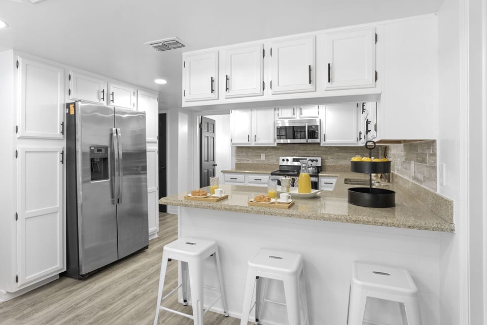 Large kitchen with cabinets, four burner stove and oven, microwave, kettle, large refrigerator, bar and lots of light.