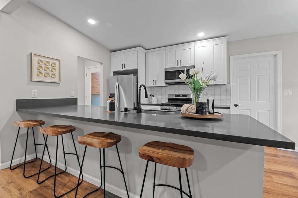 This modern kitchen boasts sleek gray countertops, white cabinetry, and stainless steel appliances. With stylish barstools and an open layout, it's a perfect space for cooking, dining, and entertaining guests.
