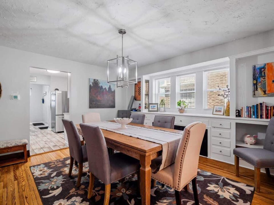 Dining room w/ long table, chandelier & windows bringing in natural light