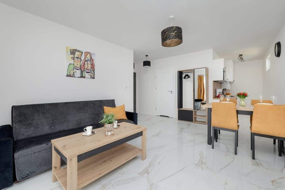 A closer look at the living room's black sofa and the wooden coffee table. The room’s neutral tones are complemented by a small, colorful painting on the wall, creating a cozy atmosphere.