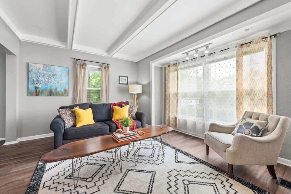 Bright living room w/ sofa seating, colorful accents & large windows letting in natural light