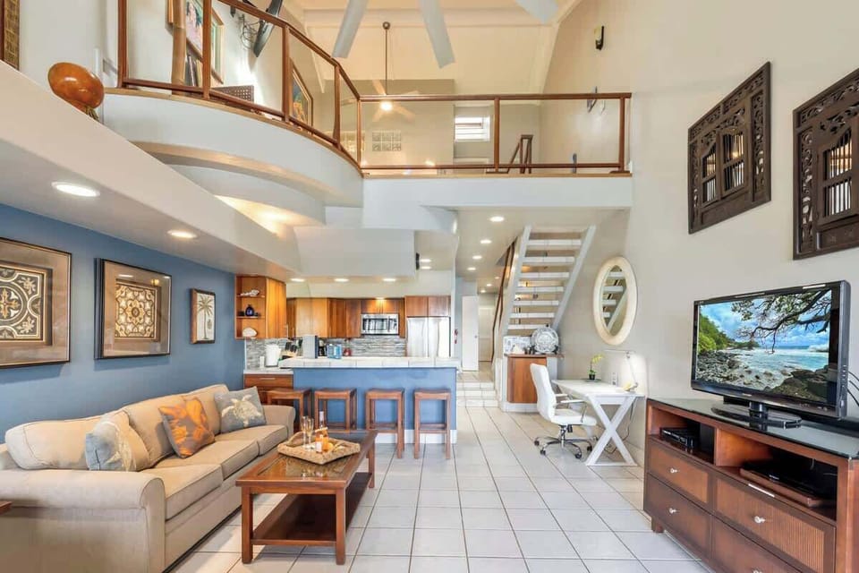 Living room features plenty of recessed lighting, TV with cable, work desk, breakfast bar, sofa sleeper, and artwork throughout. 