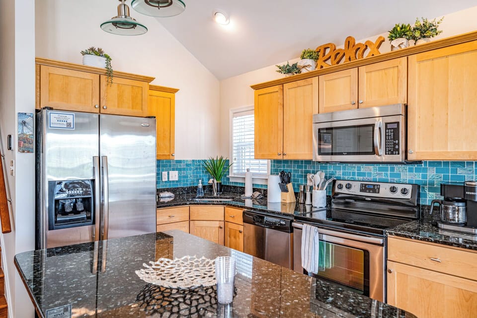 Fully equipped kitchen with stainless steel appliances and coastal backsplash