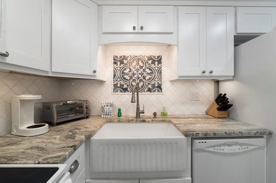 Farmhouse sink framed by new countertops, cabinets, and a designer tile backsplash.