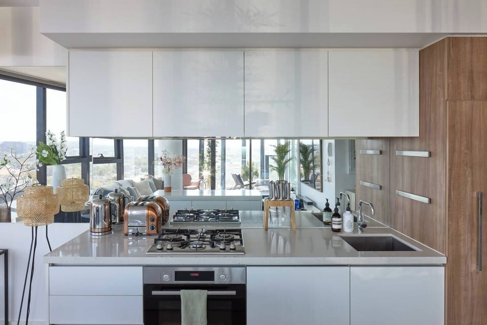 The sleek kitchen designs feature a mirrored splashback, island benchtop, copper and polished stainless steel appliances and flush cabinetry. 
