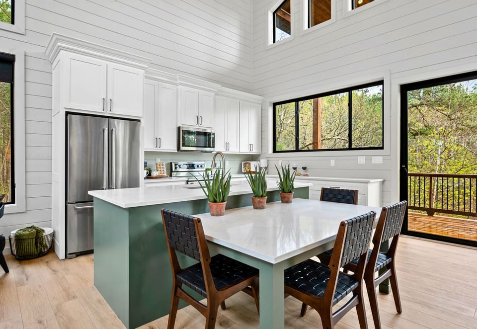 A sleek, fully stocked kitchen with white cabinetry and a deep green island creates a stylish yet functional space for cooking and entertaining.