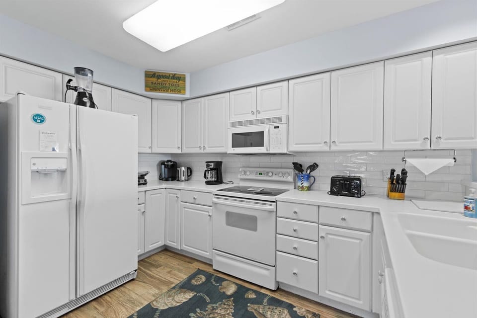 Spacious kitchen with dishwasher, electric range and oven, refrigerator, coffee pot, electric kettle, blender, and lots of supplies