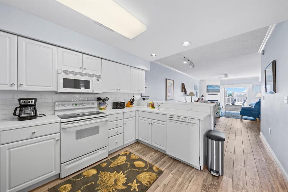 Spacious kitchen with dishwasher, electric range and oven, refrigerator, coffee pot, electric kettle, blender, and lots of supplies