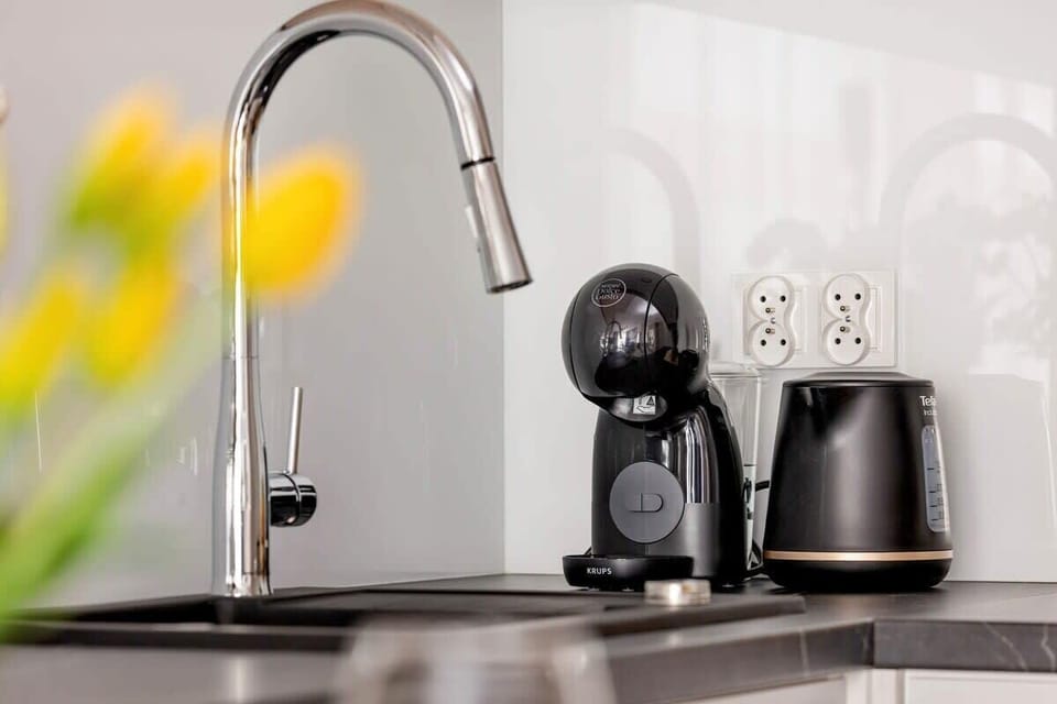 A glossy tap in a modern kitchen, alongside a sleek coffee machine and kettle, creates a stylish corner for preparing your favourite drinks.