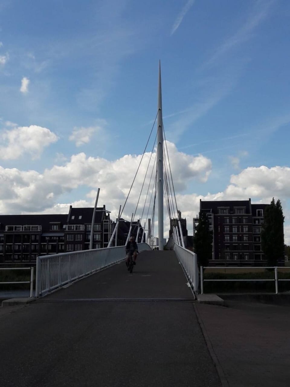 A modern pedestrian bridge with sleek architectural design, surrounded by urban residential buildings under a blue sky with scattered clouds.