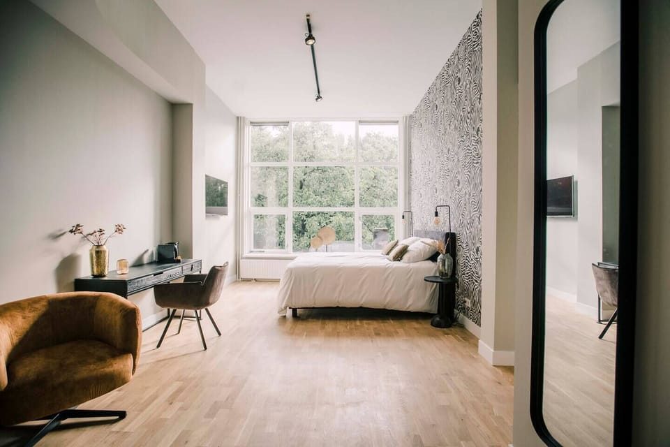 A spacious, modern bedroom with floor-to-ceiling windows, zebra-print accent wall, cozy furnishings, a sleek desk, and warm lighting for a serene atmosphere.