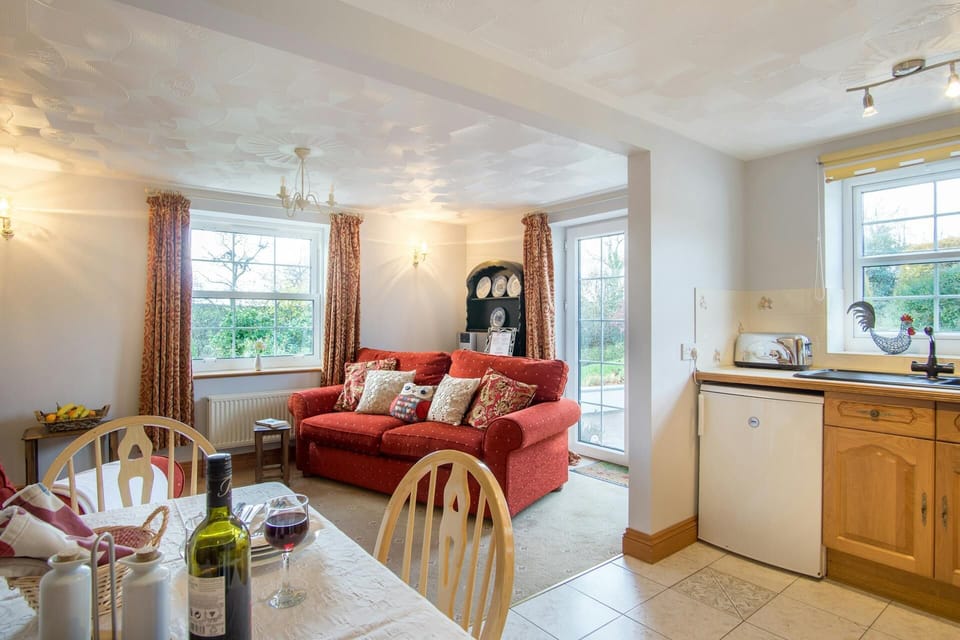 Open plan living area with sofa, patio doors and kitchen/dining area: fridge, toaster, dining table and chairs