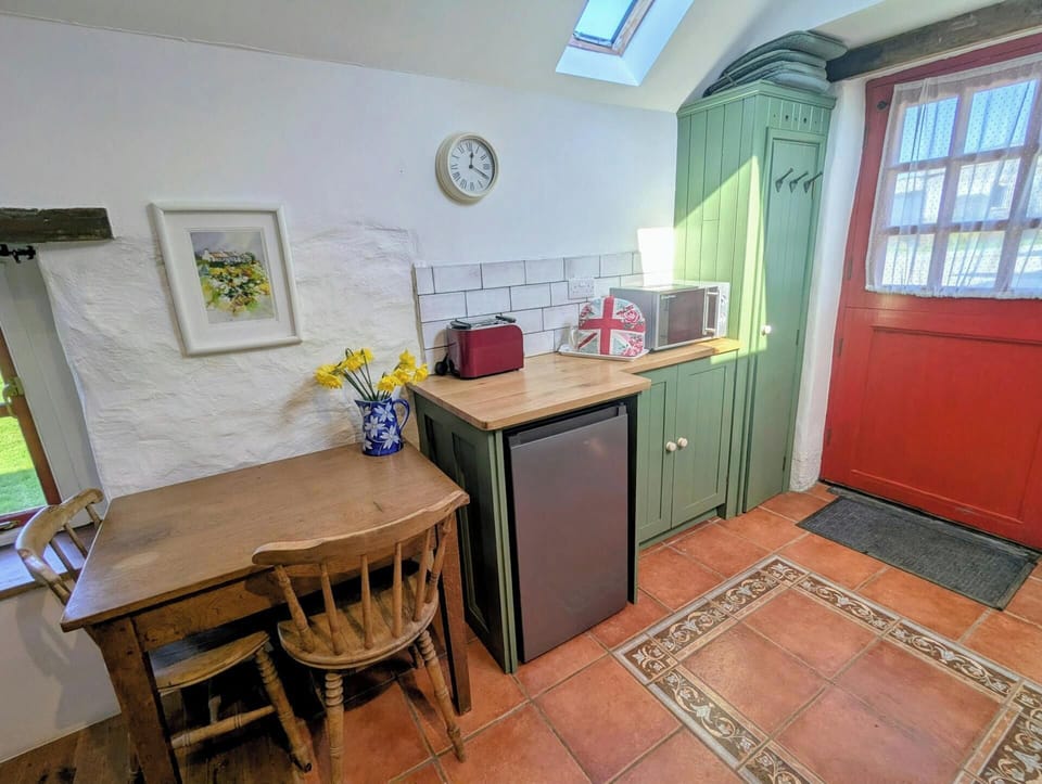 Wooden table and chair beside small fridge and countertop in a cottage kitchen