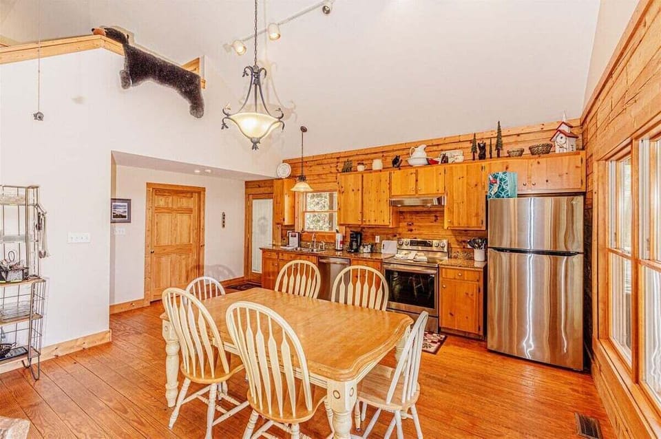 Dining table positioned beside the kitchen with wood cabinetry, stainless steel appliances, and vaulted ceilings. The open floor plan connects meal preparation and dining spaces.