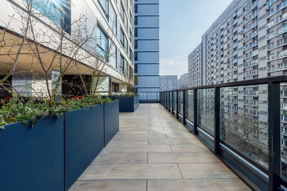 A beautifully designed balcony with black planters and sleek railings, overlooking the city skyline.

