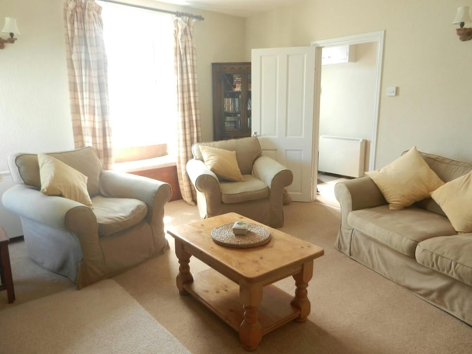 Sitting room with sofas and armchairs, coffee table, bookcase and door into hallway