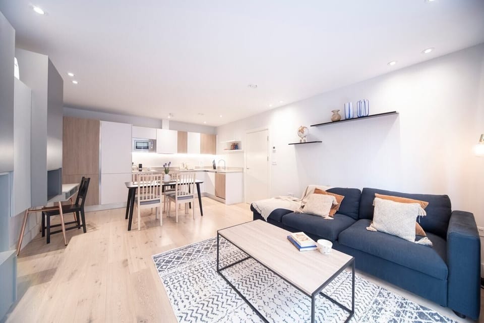 Open-plan living room with a fully equipped kitchen, sofa bed suitable for the 5th and 6th guests, a dedicated desk with a 27-inch monitor, and a smart TV.