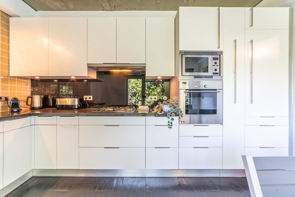 Modern white kitchen with black backsplash and stainless steel appliances — Villa Jasmine, luxury holiday villa in Herdade de Aroeira