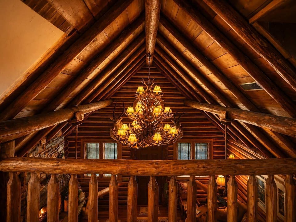 Look up to admire the incredible log craftsmanship and the grand antler-style chandelier, casting a warm, golden glow across the soaring vaulted ceilings.