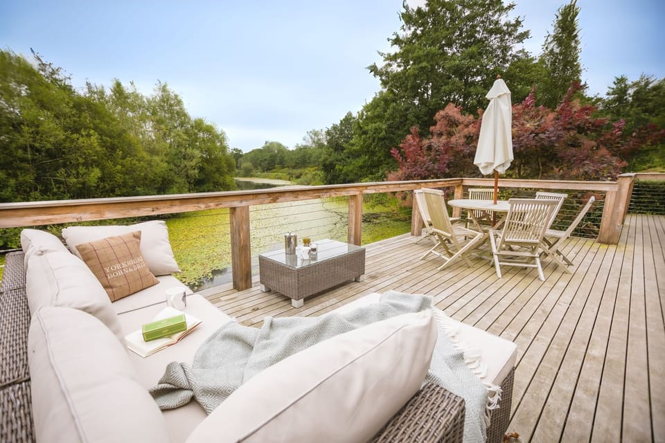 Deck at Isabella with outdoor seating, a table with chairs and umbrella, overlooking a river surrounded by trees.