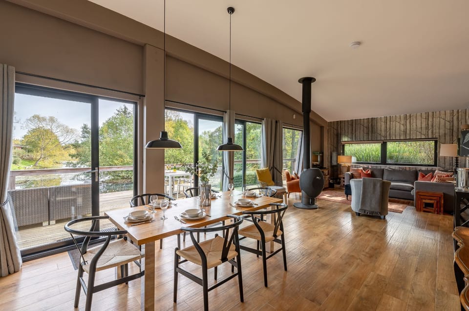 Open-plan dining and living area at Willow, large patio doors, a cosy wood-burning stove, and direct access to the lakeside decking.