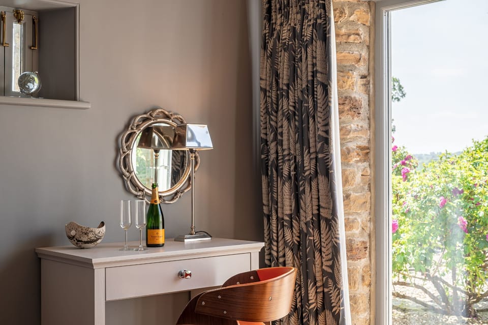 Elegant dressing area at Wayside Cottage with a vanity table, decorative mirror, champagne glasses, and views out to the garden through French doors.