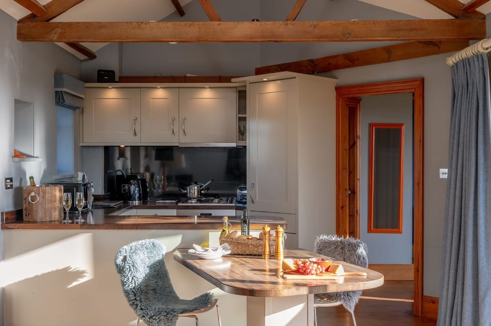 Bright kitchen area at Wayside Cottage with breakfast bar, wooden dining table, and exposed beams creating a cosy, modern-rustic feel