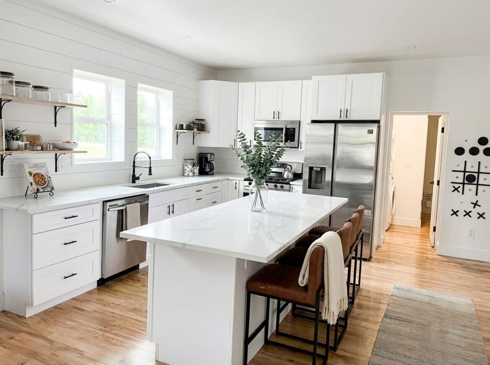 Fully stocked kitchen with gas range, stainless steel appliances, quartz counters, and open shelving