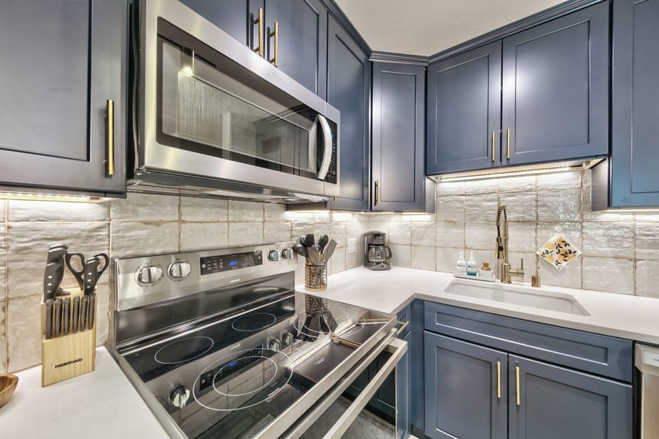 Your fully-equipped kitchen invites culinary adventures with gleaming stainless steel appliances, elegant navy cabinetry, and warm under-cabinet lighting.