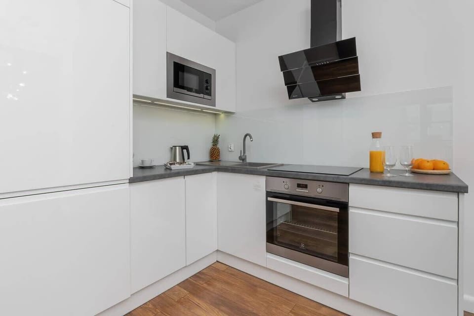 A modern white kitchen with built-in appliances and a small counter with oranges.