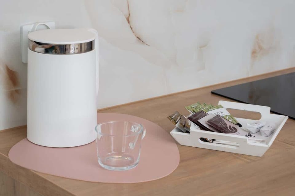 A modern electric kettle with a minimalist design sits on the kitchen counter. Its sleek, white finish complements the bright kitchen decor.