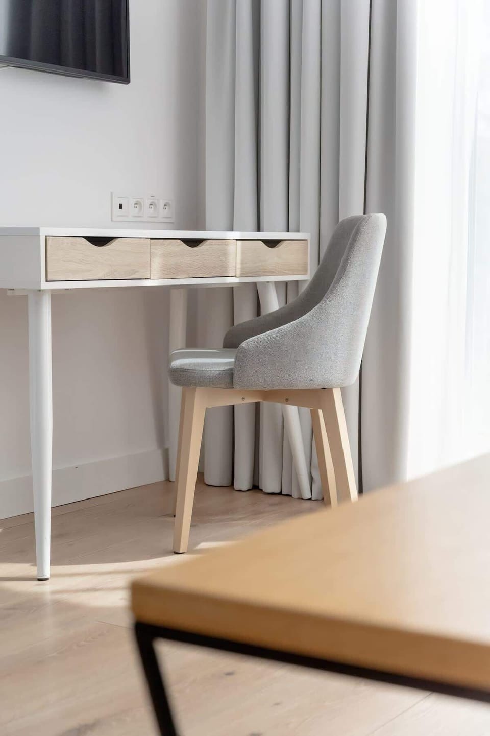 A minimalist living room setup with a table, chair, and partial view of a desk. Great for working remotely in a bright environment.